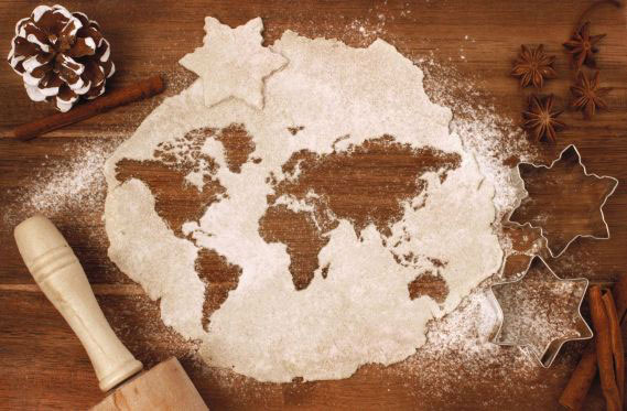 Auf einer Holzarbeitsfläche liegt ein Stück weihnachtlicher Keksteig, aus dem Kekse in Form der Kontinente ausgestochen wurden.