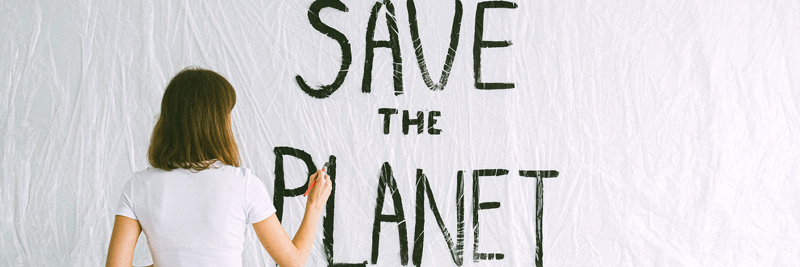 Eine Frau schreibt mit schwarzer Farbe und einem Pinsel den Schriftzug "Save the Planet" auf eine weiße Wand.