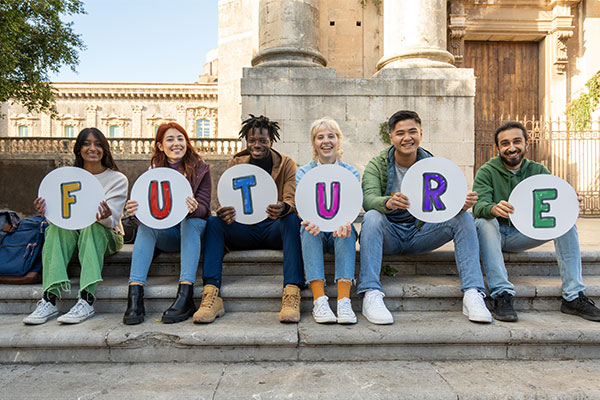 Eine Gruppe von 6 Jugendlichen sitzt auf einer Treppe im Freien. Jede Person hält einen Buchstaben in der Hand, so entsteht das Wort Future.