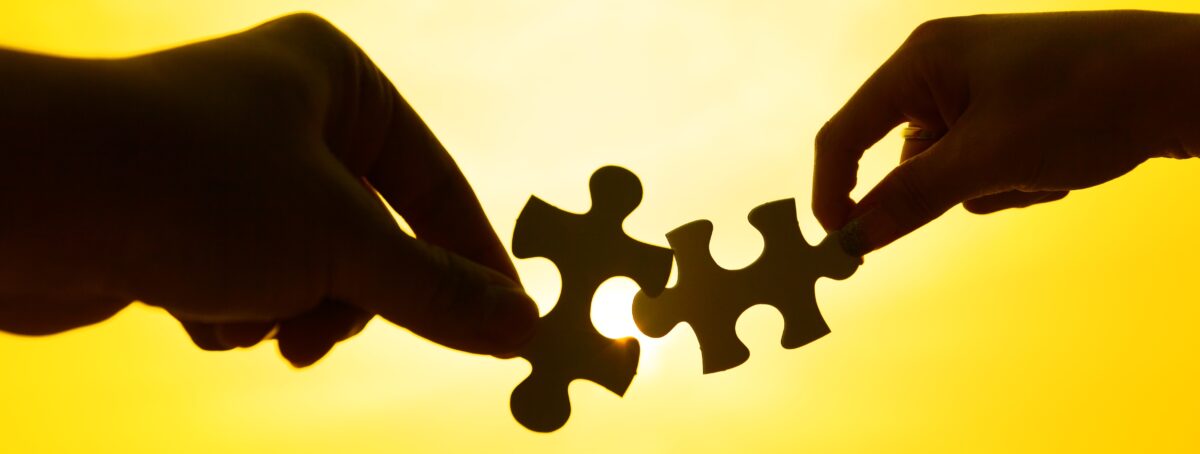 silhouette of two hands connect puzzle together